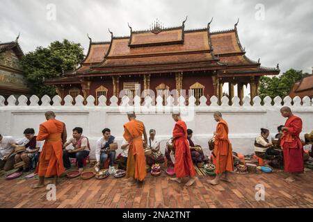 Buddhist monks receiving alms on Sisavangvong Road at dawn; Luang Prabang, Luang Prabang, Laos Stock Photo