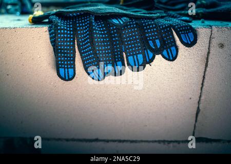 New fabric rubberized construction gloves on aerated concrete brick close-up. Purchased protective gloves for workers Stock Photo