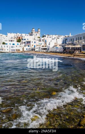 Waterfront of Naoussa with beach, restaurant patio and traditional white buildings; Naoussa, Paros Island, Cyclades, Greece Stock Photo