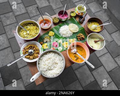 traditional south indian food platter with rice in a banana leaf and a variety of dishes arranged in a table Stock Photo