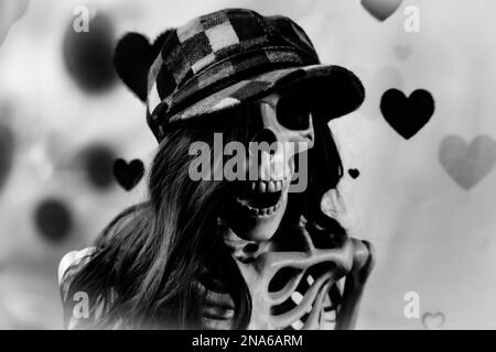 Black and white of a happy Female Skeleton Wearing a long brown wig and checkered hat for Valentine's Day Stock Photo