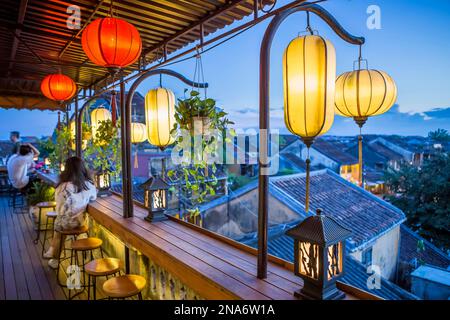 Tourists walk down the colonial streets in historic old town Hoi An. Chinese lanterns illuminate the walkways as tourists watch the sunset from a r... Stock Photo