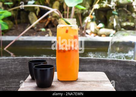 Bottle with fresh homemade juice made of oranges, watermelon, lime on the wooden table with cups Stock Photo