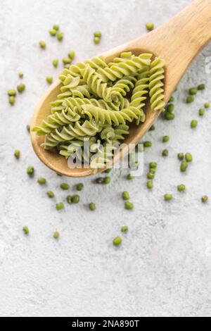 Mung bean fusilli pasta on a gray concrete background. Spoon with raw pasta and green mung bean. Gluten free pasta. Stock Photo