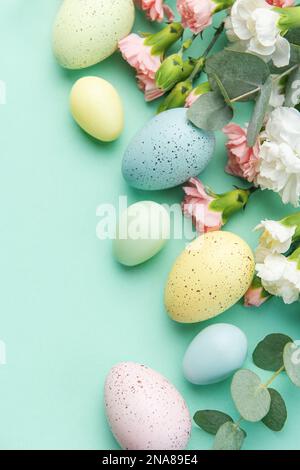 Easter colored eggs and a bouquet of white and pink carnations with eucalyptus branches on a soft green background. Festive background. Stock Photo