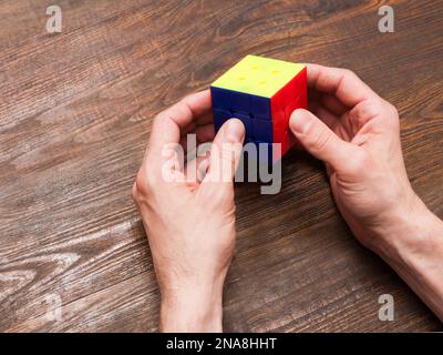 Man plays a cube of Rubik on wooden background Stock Photo