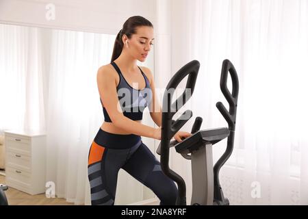 Woman using modern elliptical machine at home Stock Photo