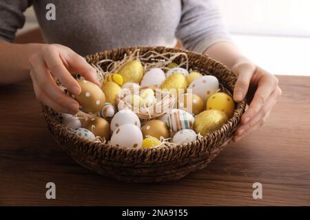Woman with basket full of dyed Easter eggs at wooden table, closeup. Easter celebration Stock Photo