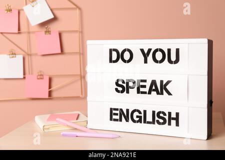 Stand with question Do You Speak English and stationery on table near pink wall Stock Photo
