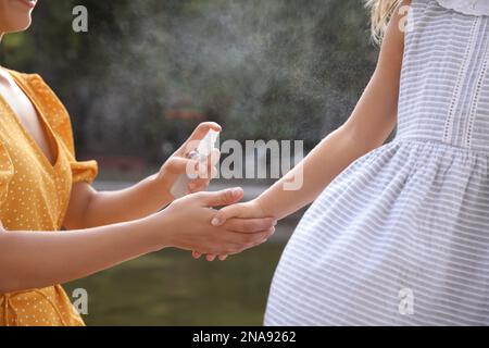 Mother applying insect repellent onto girl's hand outdoors, closeup Stock Photo
