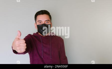 A Young man with face mask making thumbs up sign Stock Photo