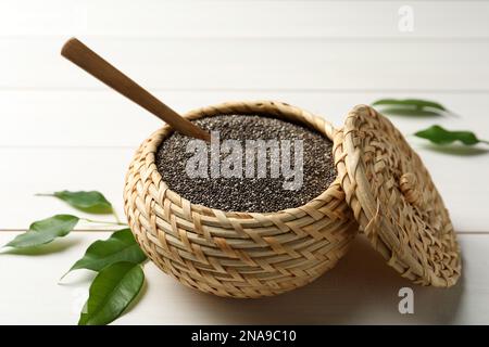 Wicker box with chia seeds and spoon on white wooden table Stock Photo