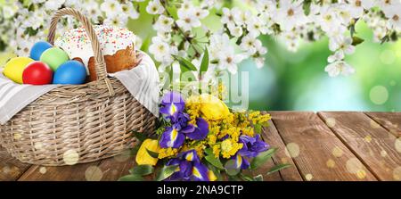 Basket with traditional Easter cake, eggs and flowers on wooden table outdoors, space for text. Banner design Stock Photo