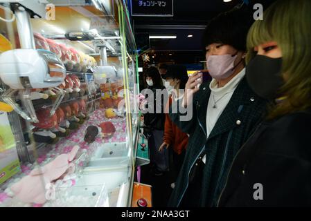 Japanese teenagers trying to pick toys in a toy crane claw machine in ...
