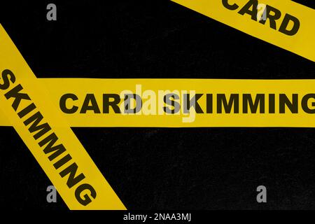 Card skimming cybercrime and theft alert, caution and warning concept. Yellow barricade tape with word in dark black background. Stock Photo