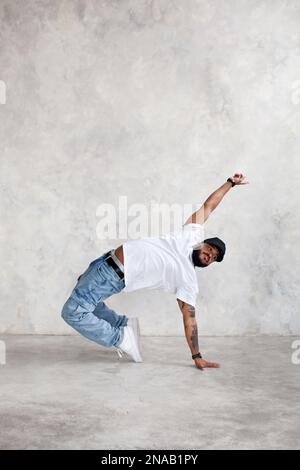 Man dancing break dance against background of gray wall in studio. Cool guy dancer, copy space Stock Photo
