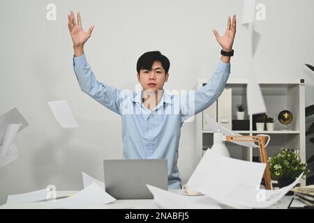 Stressed man office worker sitting at desk and throwing paperwork in the air, feeling distressed anxious with work deadline Stock Photo