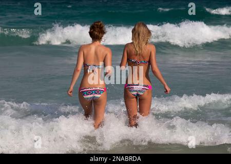 Girls in matching bikinis walk into the ocean. Stock Photo