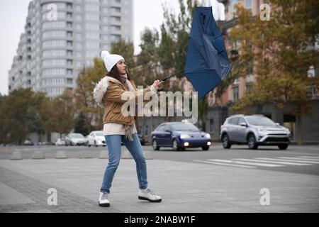 Woman with blue umbrella caught in gust of wind on street Stock Photo