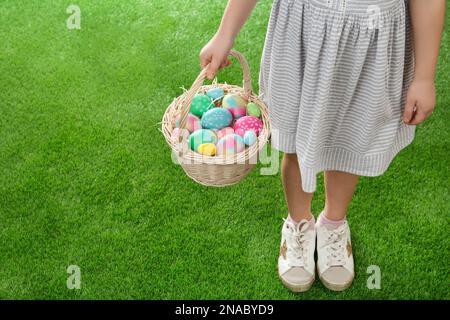 Little girl with basket full of Easter eggs on green grass, closeup. Space for text Stock Photo