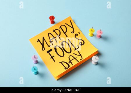 Sticky note with phrase Happy Fools' Day and push pins on light blue background Stock Photo
