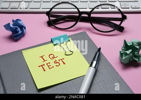 Sticker note with text IQ Test, notebook, pen, crumpled paper balls, keyboard and glasses on pink background, closeup Stock Photo