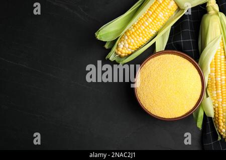 Cornmeal in bowl and fresh cobs on black table, flat lay Stock Photo