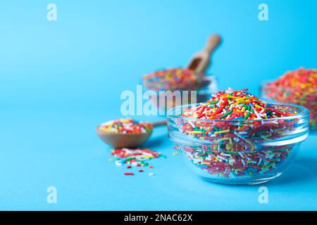 Colorful sprinkles in bowl on light blue background, space for text. Confectionery decor Stock Photo