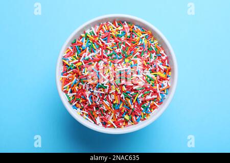 Colorful sprinkles in bowl on light blue background, top view. Confectionery decor Stock Photo