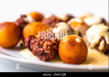 Baked meatball with fried croquette in cheese lemon sauce on white plate, closeup. Stock Photo