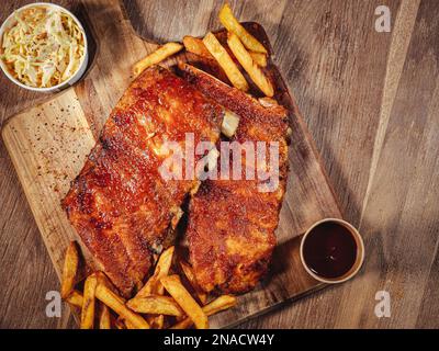 grilled pork ribs with french fries and sauces served on a wooden cutting board, view from top Stock Photo