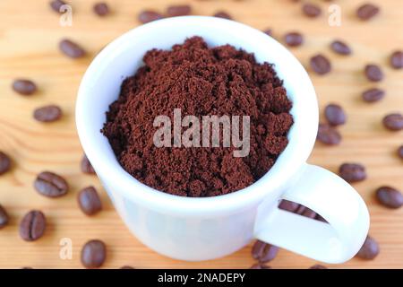 Cup of Ground Coffee on Wooden Table with Scattered Roasted Coffee Beans Stock Photo