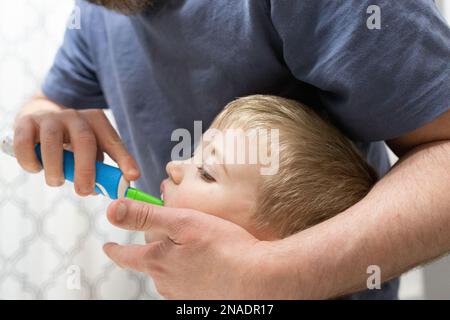Close-up of Father Helping Son Brush Teeth with Electric Toothbrush Stock Photo