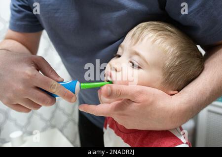 Dad Helps Child Brush Teeth with Colorful Electric Toothbrush Stock Photo