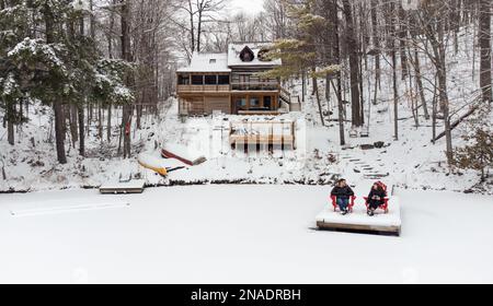 Couple sitting in chairs on end of snowy dock on winter day. Stock Photo