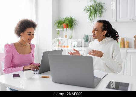 Positive african american woman using laptop while boyfriend talking at home Stock Photo