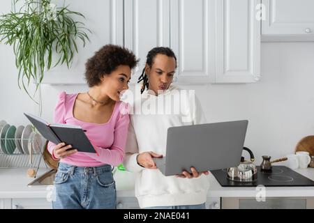 African american couple working with laptop and notebook in kitchen Stock Photo