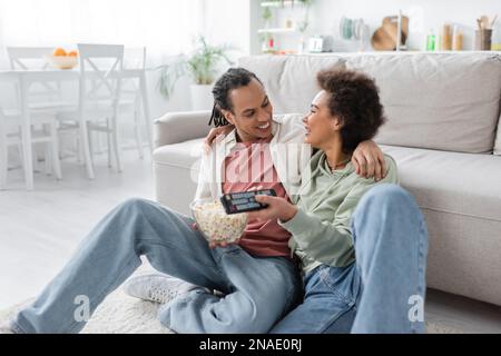 Positive african american couple with popcorn hugging while watching movie at home Stock Photo