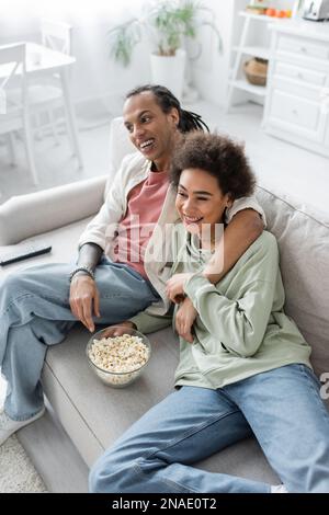 Smiling african american couple sitting near popcorn and remote controller on couch Stock Photo