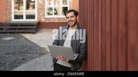 young man with a laptop in his hands smiling looking at the camera outside. Stock Photo