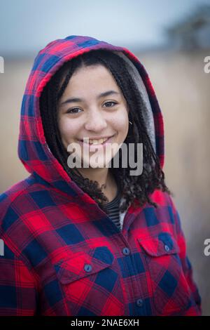portrait of biracial young woman smiling with braids and hood Stock Photo