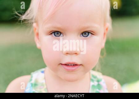 Face of baby girl two years old plays on the grass, summer Stock Photo