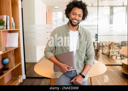 Smart and ambitious african-american male office employee posing with laptop indoor, friendly black business woman looking at the camera and smiles, beginner full of inspirations first day at work Stock Photo