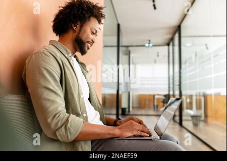 Portrait of concentrated african-american male employee using laptop computer, smiling black businessman responds emails, freelancer woman working on the distance sitting in coworking space, side view Stock Photo