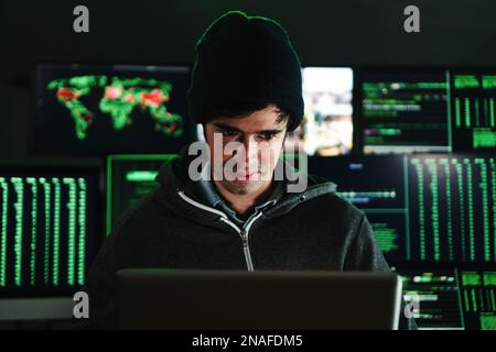 Concentrated hacker man, programmer or developer typing software code on a laptop computer at background a lot of screens with text. Cyber security concept. High quality photo Stock Photo