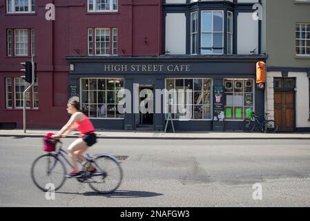 Cyclist rides by a cafe along a street in Oxford, UK; Oxford, England Stock Photo