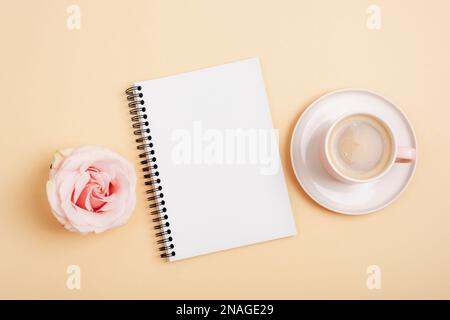 Coffee in cup, rose flower and spiral notebook on neutral background. Top view, flat lay, mockup. Stock Photo