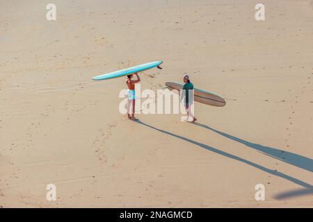 Two friends standing in the sand near the ocean, each holding a surfboard Stock Photo