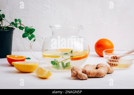 Glass teapot with orange, lemon, ginger and mint tea with ingredients against white background, closeup. Stock Photo