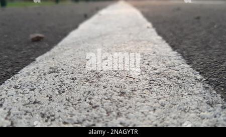 Road surface with white line close-up. Texture of gray asphalt and road markings closeup. Smooth view of the stadium sports area. Stock Photo